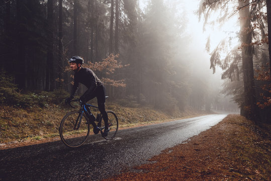 Rennradfahrer im Wald bei herbstlichem Wetter mit Sonnenstrahlen im Nebel