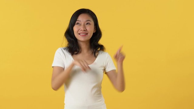 Young happy smiling Asian woman in white t-shirt opening hands and pointing left right against yellow background
