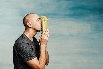 Funny bald man looks at celery, as if praying for it, against a blue background. Kisses the food.