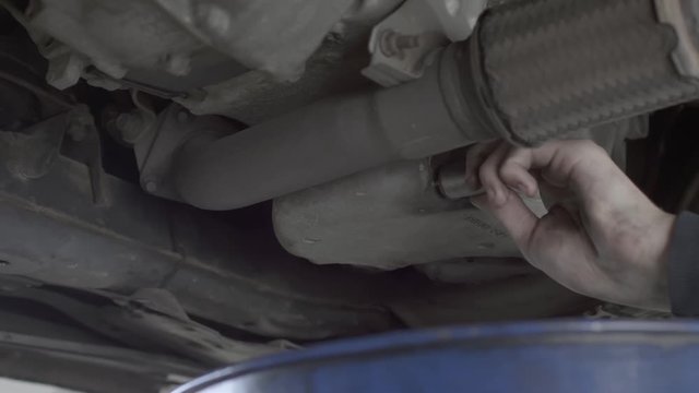 Car in a mechanic workshop being repaired. The car mechanic unscrews the crankcase screw. The oil is leaking out.