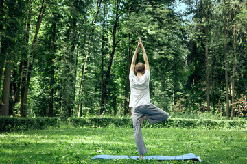 Fitness, man training yoga in tree pose in park. Young sporty guy makes breathing exercise standing...