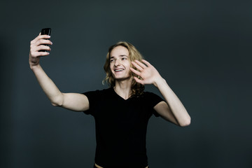 Young man with long blonde hair makes a selfie on a black background.