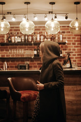 Beauty young woman in hooded coat portrait at a night bar alone