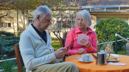 Caucasian retired couple having breakfast and playing cards in the garden