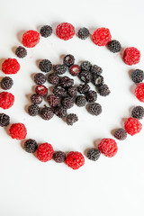 Red and black raspberries laid out in a circle on a white background.