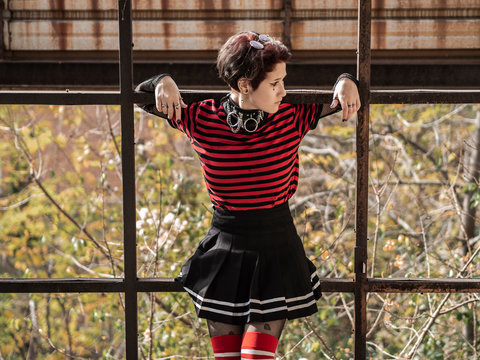 Goth punk girl portrait with a skirt and striped stockings chilling out on rusty metal structures in an abandoned factory. A young generation of alternative teens concept