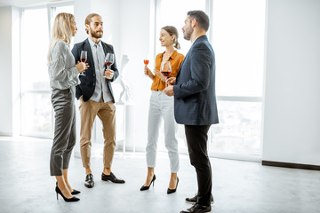 Young elegantly dressed people meeting in the white hallway or showroom, talking and drinking wine...