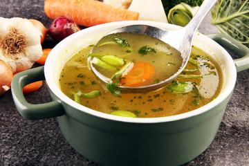 Broth with carrots, onions various fresh vegetables in a pot - colorful fresh clear spring soup....