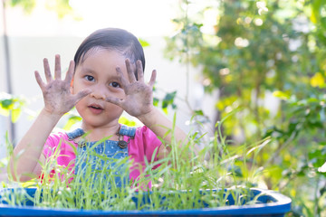 Adorable 3 years old show her dirty hands during planting the vegetable in the garden outside the house, concept of learning activity for kid development.