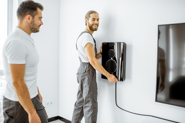 Two professional workmen in workwear installing luxury audio system in the white living room. Home...