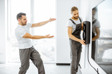 Two professional workmen in workwear installing luxury audio system in the white living room. Home appliances installation concept