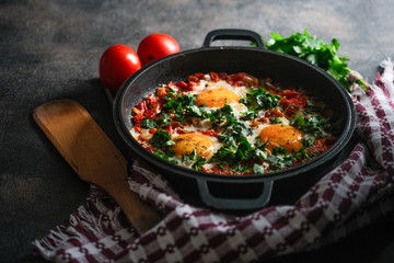 Traditional  shakshuka with eggs, tomato, and parsley in a iron pan on a dark background