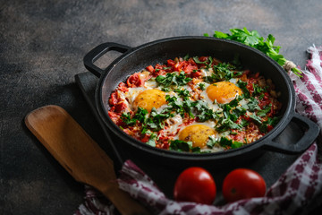 Traditional  shakshuka with eggs, tomato, and parsley in a iron pan on a dark background