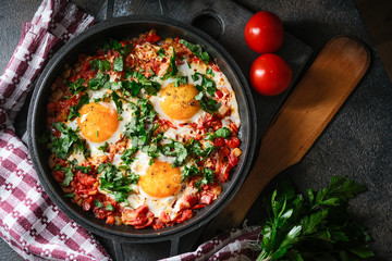 Shakshuka with eggs, tomato, and parsley in a iron pan. Top view copy space