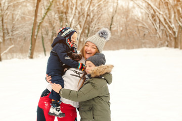 Happy kids hugging their mother outdoors in winter