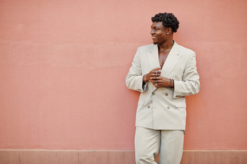 Stylish afro man in beige old school suit against pink wall. Fashionable young African male in casual jacket on bare torso.