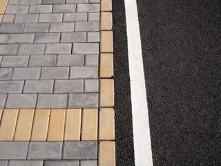 Top view photo of a fragment of a sidewalk paved with grey and yellow tiles and a bicycle lane with rubber coating.