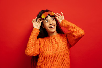 African-american young brunette woman's portrait in ski mask on red studio background. Concept of human emotions, facial expression, sales, ad, winter sport and holidays. Looking up, smiling.