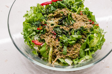 Homemade Salad with Herbal Sauce and Red Pepper Slices Mixed with Two Spoon in Glass Bowl.