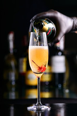 Fototapeta premium bartender pours bellini champagne cocktail into a glass with cherry