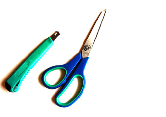 Green stationery knife and blue scissors on a white isolated background. Place for text.