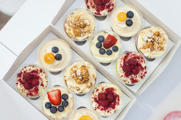 Box of assorted cupcakes with cream cheese vanilla and chocolate frosting, fresh strawberries, raspberries, blueberries and popcorn decoration. 