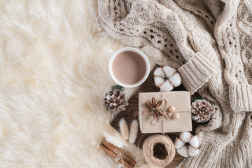Autumn or winter composition. Gift box Coffee cup, cinnamon sticks, anise stars, beige sweater with knitted blanket on cream color gray fluffy background. Flat lay top view copy space.