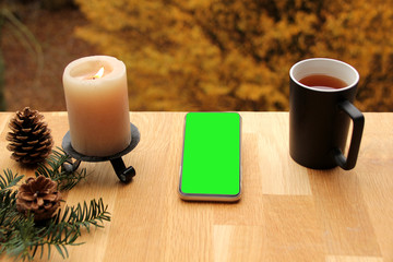 on a wooden table vertically lies a modern telephone with pre-keyed green screen, on the right is a...