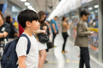 Smart looking, confident Asian preteen boy wear white t-shirt, backpack, wait for underground train in crowded platform in the morning, Routine commute of school student, city lifestyle, life skills. 