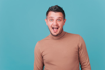 Portrait of happy cheerful playful fashionable man with appealing smile in beige sweater look at cam on blue background. Positive funny emotions, white teeth, laugh happily. Lifestyle concept