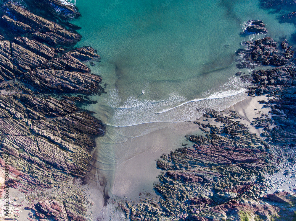 Wall mural aerial view of person swimming in a bay with rocks