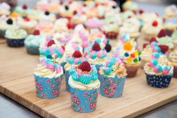 Assorted colorful cupcakes with blue, pink and orange frosting, decorated with raspberries, marshmallow, sprinkles and candies. 