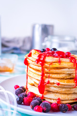 Pancakes with red fruits stacked with raspberry jam on a white plate.