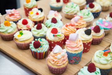 Assorted colorful cupcakes with blue, pink and orange frosting, decorated with raspberries, marshmallow, sprinkles and candies. 
