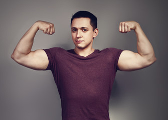 Naklejka premium Young casual strong man showing biceps on the arms on grey background. Closeup