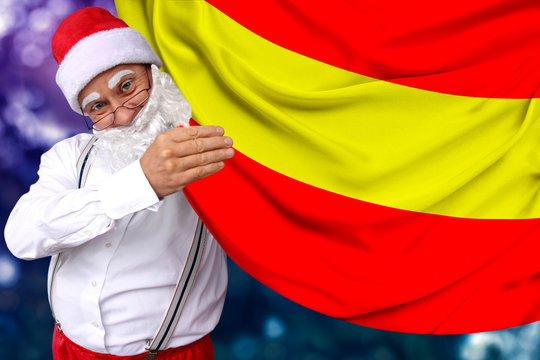 Santa Claus with a beard holds the beautiful colored national flag of the state of Spain on fabric, concept of tourism, New Year and Christmas, economic and political prospects