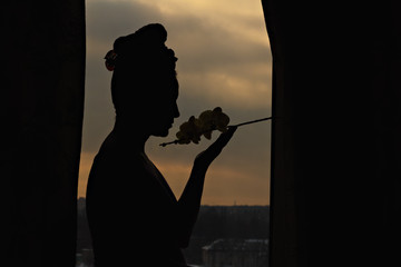 Female silhouette with a flower in the window at sunset. Life style