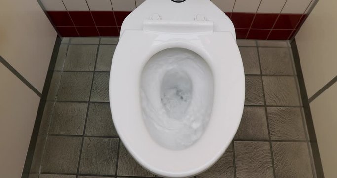 From above clean water flushing in white toilet in public water closet