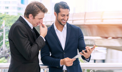Business people meeting and sharing their ideas while looking tablet pc in their hands. Business young men talking about planning work outside office building background.Business togetherness concept.