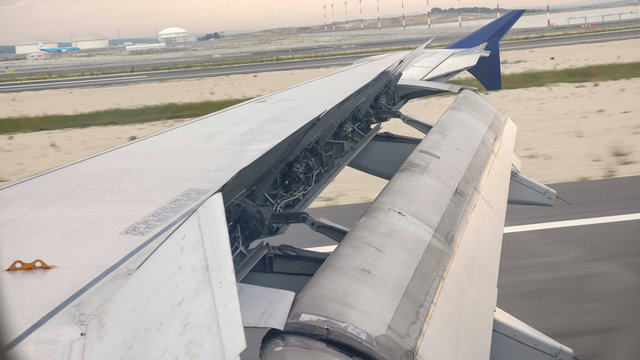 Plane landing on the runway, detail of wing, spoilers and ailerons. Aircraft wing outside board aileron lifting up for maneuvering speed while take off at the airport.