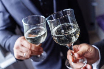 Close up portrait of a male's hands toasting with glasses of wight wine over table