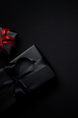 black gift box with red and black ribbons isolated on black background