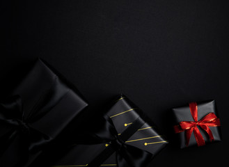 black gift box with red and black ribbons isolated on black background