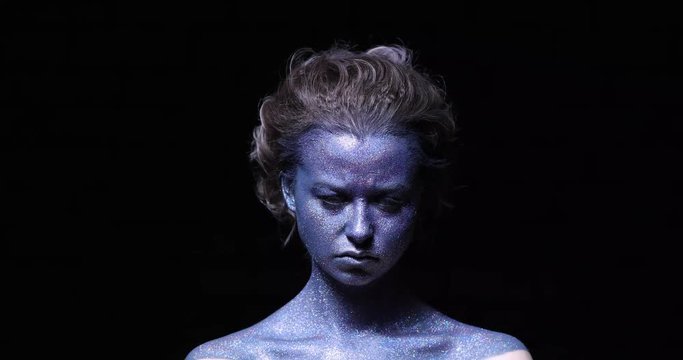 girl with a blue face in sparkles frowns at the camera