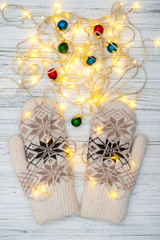 Winter mittens with an ornament and with decorative bulbs or with a New Year's garland on a textured white table