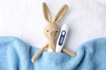 Toy bunny with thermometer on towel background, top view