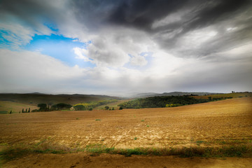 Fototapeta premium Dark clouds over a brown field in Tuscany
