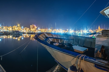 Boat with Alghero sea front on the background at night