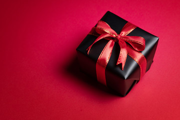 Top view of black gift box with red and black ribbons isolated on red background.