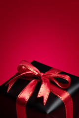 Top view of black gift box with red and black ribbons isolated on red background.